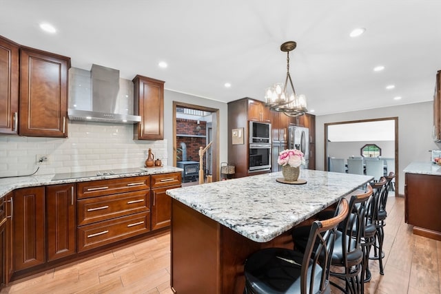 kitchen featuring a kitchen island, stainless steel appliances, light hardwood / wood-style floors, wall chimney range hood, and a kitchen bar