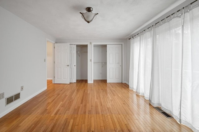 unfurnished bedroom with visible vents, baseboards, two closets, and light wood finished floors