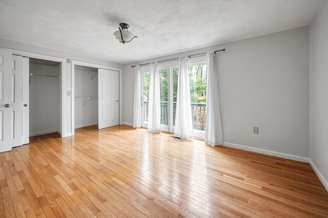 unfurnished bedroom with light wood finished floors, baseboards, multiple closets, and access to exterior