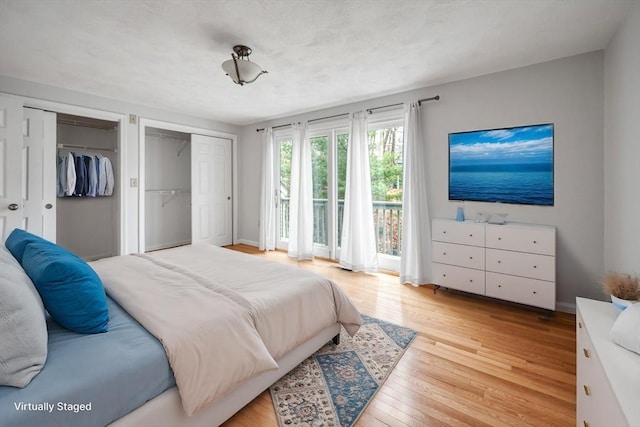 bedroom with baseboards, two closets, light wood-style floors, and access to outside