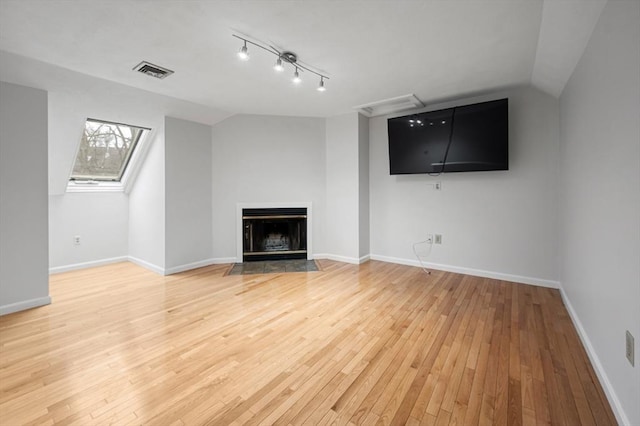 unfurnished living room with baseboards, visible vents, vaulted ceiling with skylight, a fireplace with flush hearth, and light wood-type flooring