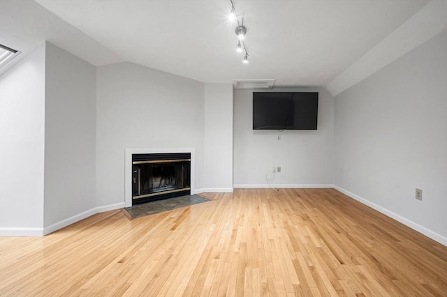 unfurnished living room featuring baseboards, light wood finished floors, a fireplace with flush hearth, vaulted ceiling, and rail lighting