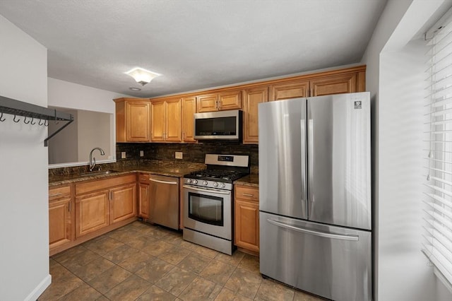 kitchen featuring decorative backsplash, dark stone countertops, brown cabinets, appliances with stainless steel finishes, and a sink