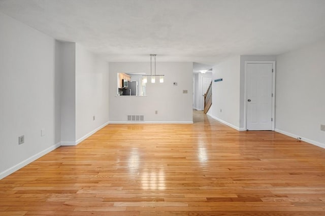 unfurnished living room with stairs, baseboards, visible vents, and light wood finished floors