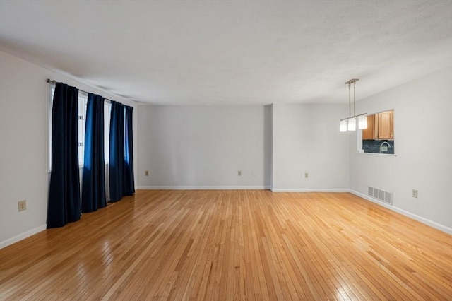 empty room with baseboards, visible vents, and light wood finished floors