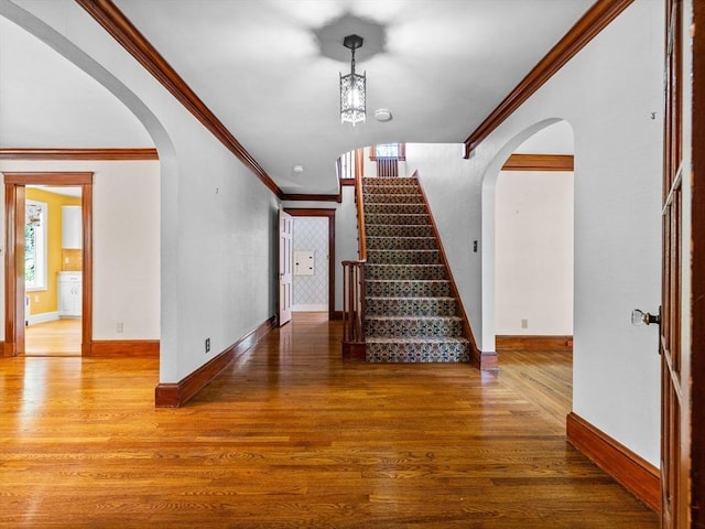 stairs with crown molding, wood finished floors, and arched walkways