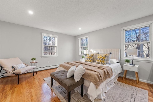 bedroom with a textured ceiling, baseboard heating, and light hardwood / wood-style flooring