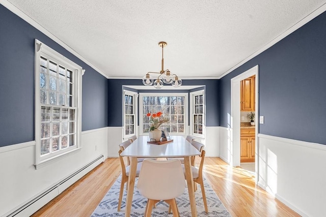 dining room with baseboard heating, a textured ceiling, crown molding, and a chandelier