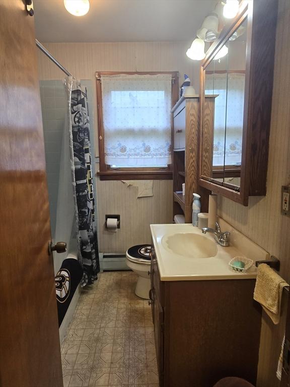 bathroom with plenty of natural light, toilet, vanity, baseboard heating, and wooden walls