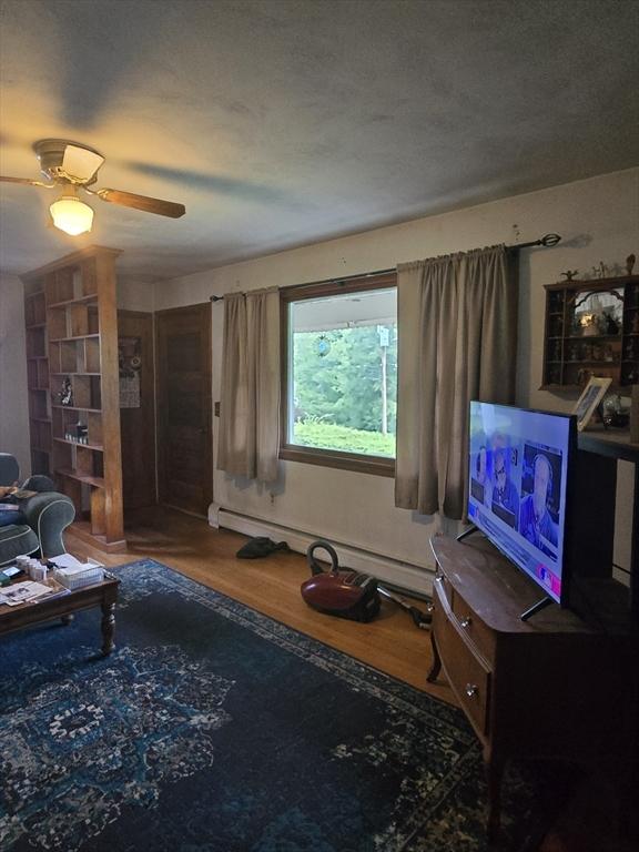 living area featuring wood finished floors, a baseboard heating unit, and a ceiling fan