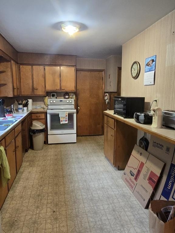 kitchen featuring black microwave, brown cabinetry, light floors, light countertops, and white electric stove