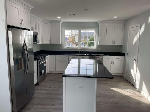 kitchen featuring dark wood-type flooring, dark stone countertops, appliances with stainless steel finishes, a kitchen island, and white cabinetry