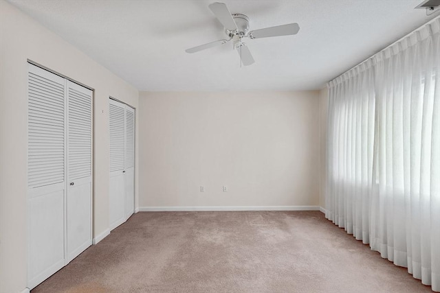 unfurnished bedroom with ceiling fan, light carpet, and two closets