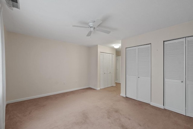 unfurnished bedroom with multiple closets, ceiling fan, and light colored carpet