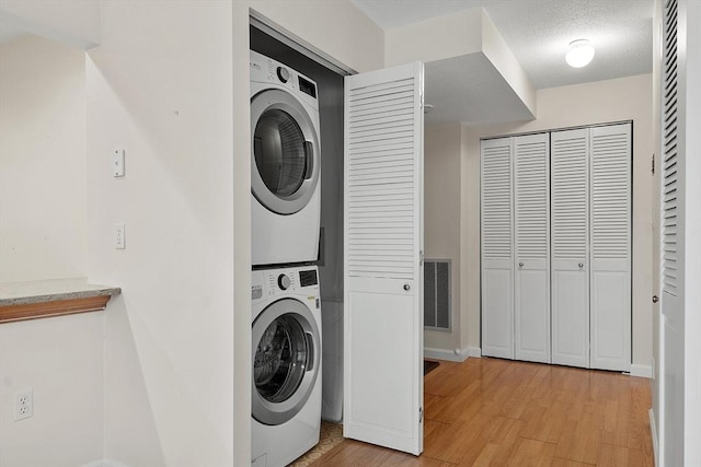 laundry room featuring stacked washer / drying machine, light hardwood / wood-style floors, and a textured ceiling