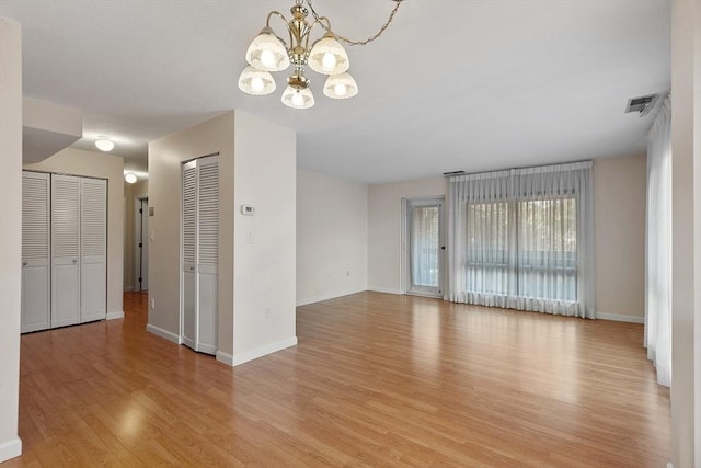 unfurnished room featuring a chandelier and light hardwood / wood-style flooring