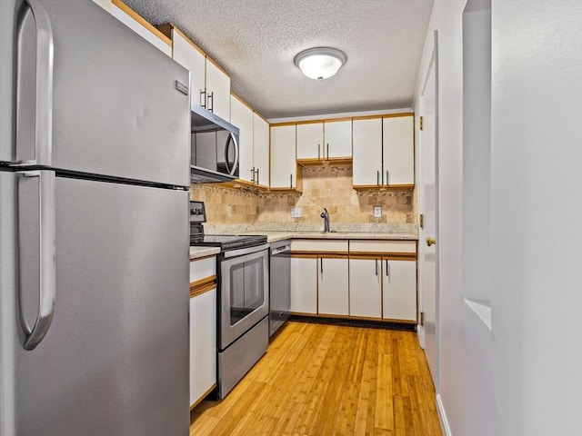 kitchen with light wood finished floors, light countertops, decorative backsplash, appliances with stainless steel finishes, and white cabinetry