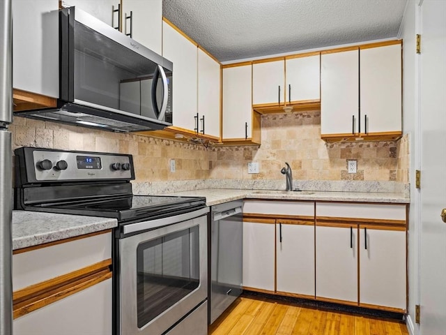 kitchen with a sink, light wood-style flooring, appliances with stainless steel finishes, and white cabinets