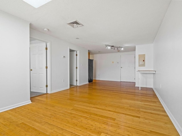 empty room with visible vents, baseboards, light wood-type flooring, electric panel, and a textured ceiling