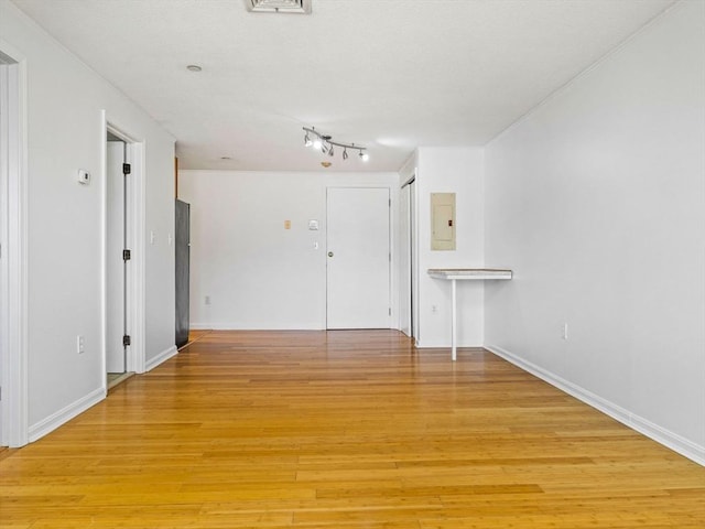 unfurnished room featuring light wood finished floors, baseboards, and electric panel