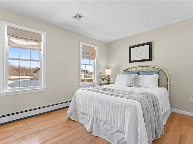 bedroom featuring a baseboard heating unit and light hardwood / wood-style floors