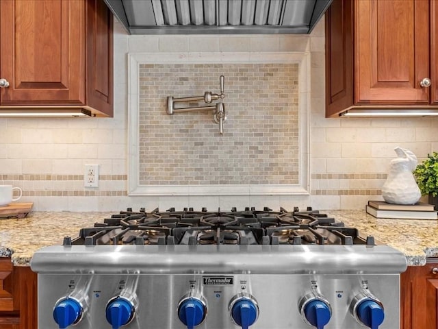 interior details featuring wall chimney exhaust hood, light stone countertops, decorative backsplash, and stove