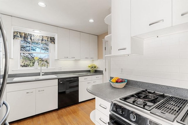 kitchen with a sink, black dishwasher, light wood finished floors, dark countertops, and stainless steel range with gas stovetop