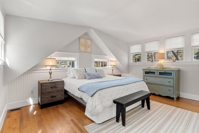 bedroom with vaulted ceiling, multiple windows, wood finished floors, and visible vents