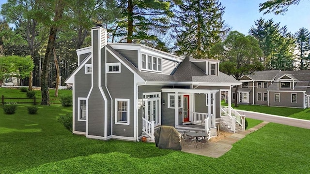 rear view of property with a shingled roof, a patio area, a lawn, and a chimney