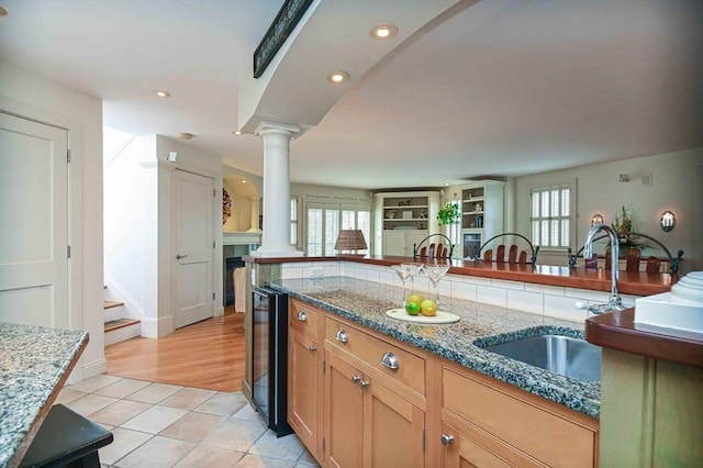 kitchen featuring decorative columns, a sink, light tile patterned floors, stone counters, and a wealth of natural light