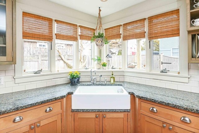 kitchen with backsplash, brown cabinetry, glass insert cabinets, and a sink