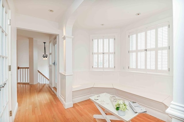 hall featuring a healthy amount of sunlight, light wood finished floors, ornate columns, and an upstairs landing