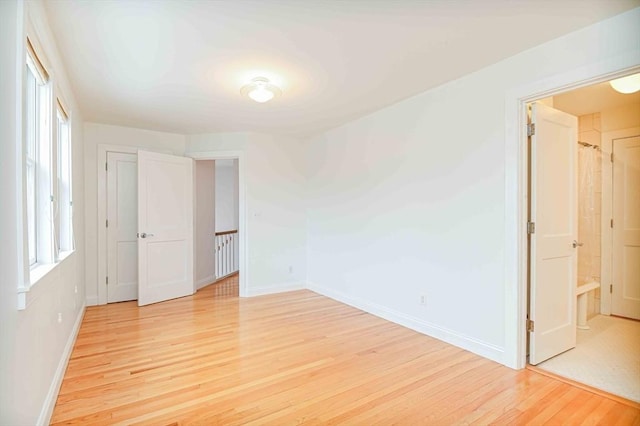 unfurnished bedroom with light wood-style floors, baseboards, and ensuite bathroom