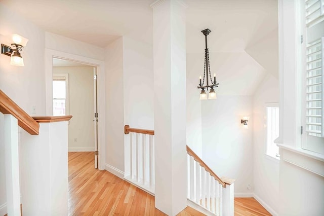 hall featuring an inviting chandelier, baseboards, light wood finished floors, and an upstairs landing