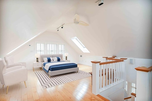 bedroom featuring track lighting, baseboards, wood finished floors, and vaulted ceiling with skylight