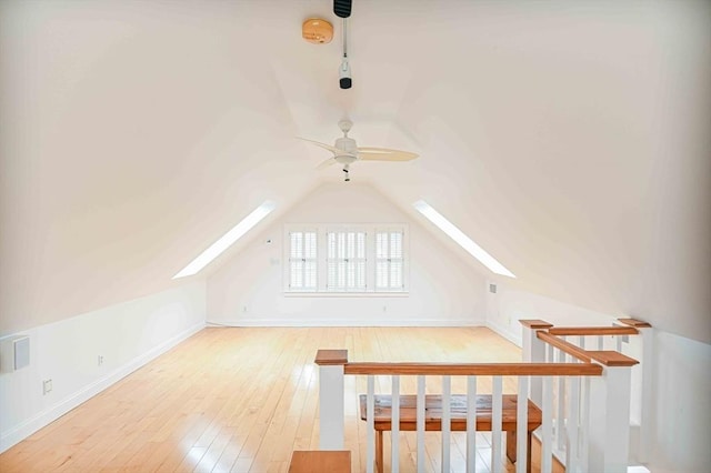 bonus room with wood-type flooring, ceiling fan, baseboards, and vaulted ceiling with skylight