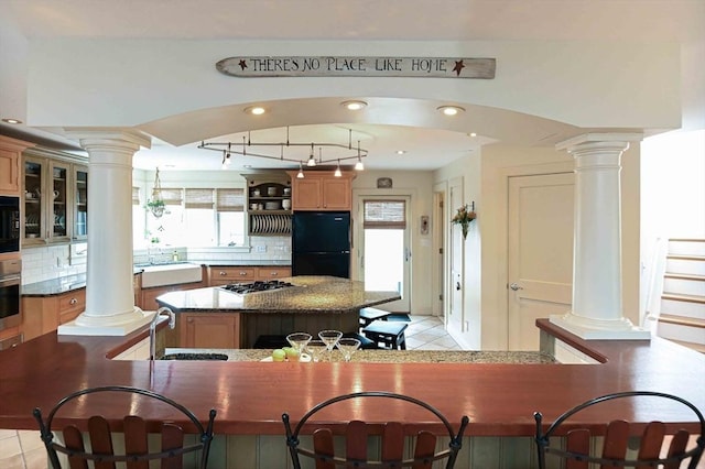 kitchen featuring a sink, backsplash, a kitchen island, ornate columns, and black appliances
