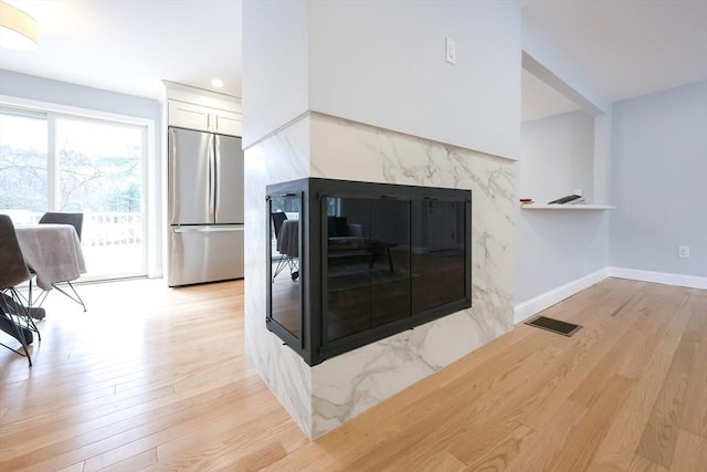 44 Dean Rd, Wayland, MA 01778 - detailed view of stainless steel refrigerator, light wood-type flooring, white cabinets, baseboards, and a high end fireplace