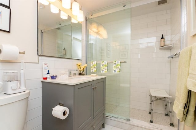 full bathroom with a stall shower, vanity, tile walls, and toilet