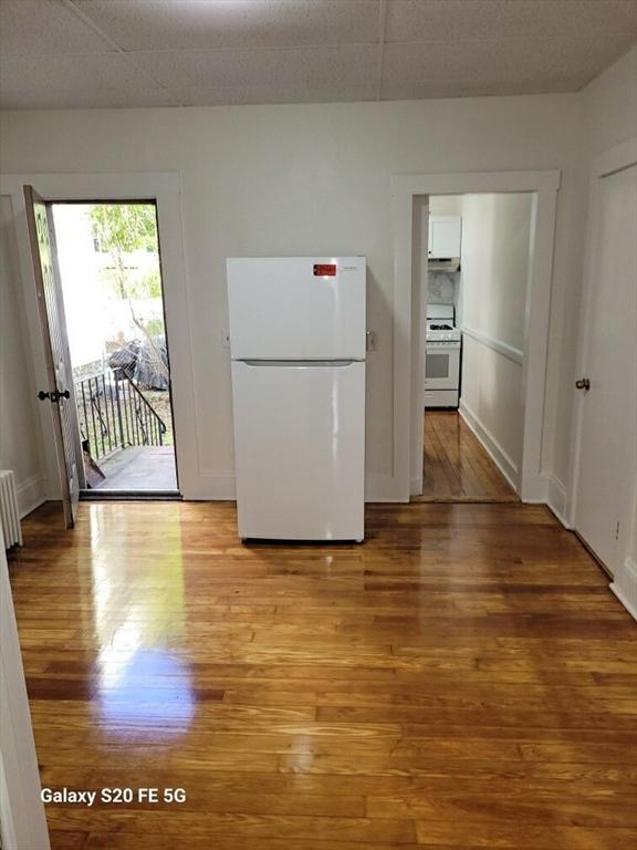 kitchen featuring a paneled ceiling, radiator heating unit, white appliances, and light wood-type flooring