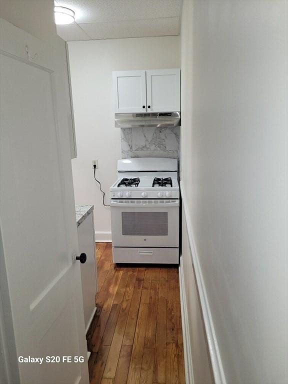 kitchen with white gas range, white cabinetry, light stone countertops, dark hardwood / wood-style flooring, and decorative backsplash