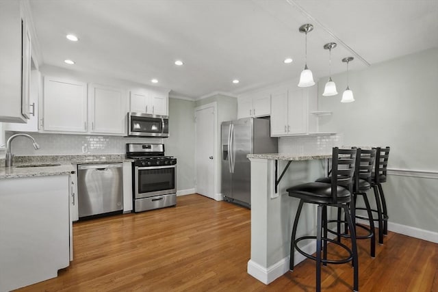 kitchen with white cabinets, appliances with stainless steel finishes, wood finished floors, a peninsula, and a sink