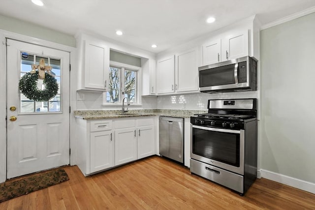 kitchen with stainless steel appliances, a sink, white cabinets, backsplash, and light wood finished floors