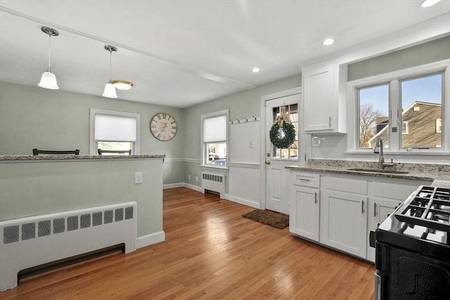 kitchen featuring hanging light fixtures, radiator heating unit, gas stove, and white cabinets