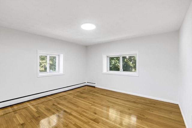 empty room featuring baseboard heating, plenty of natural light, wood-type flooring, and baseboards
