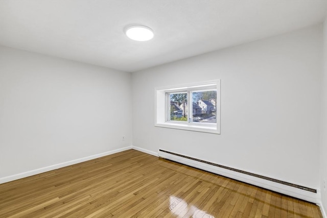 empty room featuring a baseboard heating unit, light wood-style flooring, and baseboards
