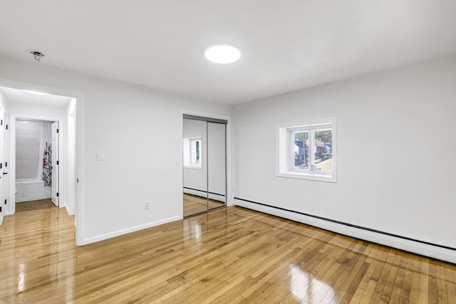 unfurnished bedroom featuring multiple windows, light wood-style floors, a baseboard radiator, and a closet