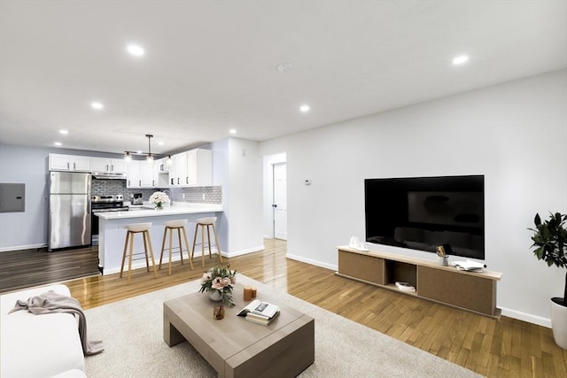 living area featuring recessed lighting, baseboards, wood finished floors, and electric panel