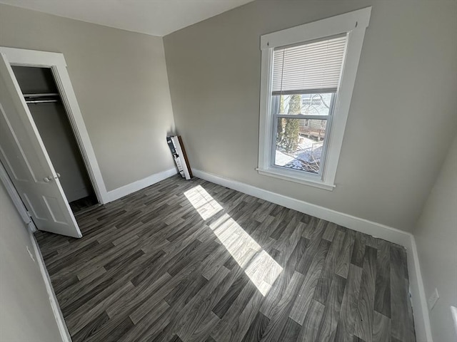 unfurnished bedroom with a closet, dark wood finished floors, and baseboards