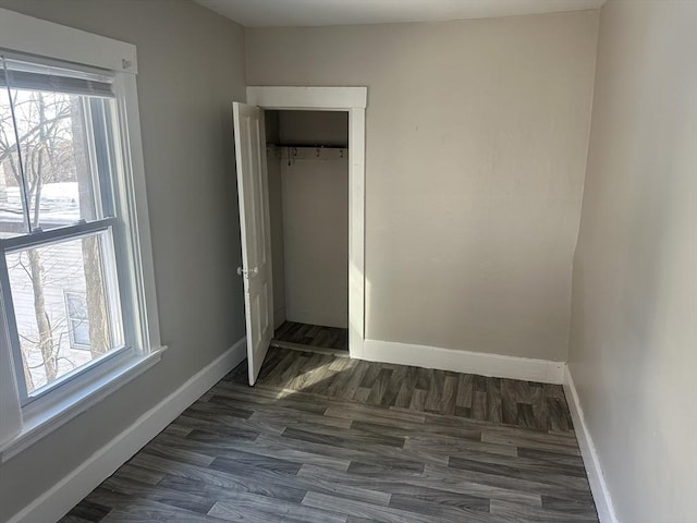 unfurnished bedroom with dark wood-style floors, baseboards, and a closet